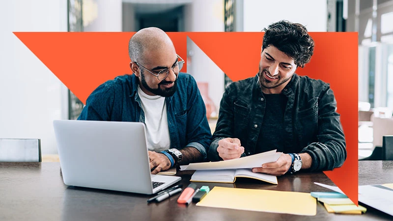 Two business owners reviewing paperwork, with orange geometric branding.